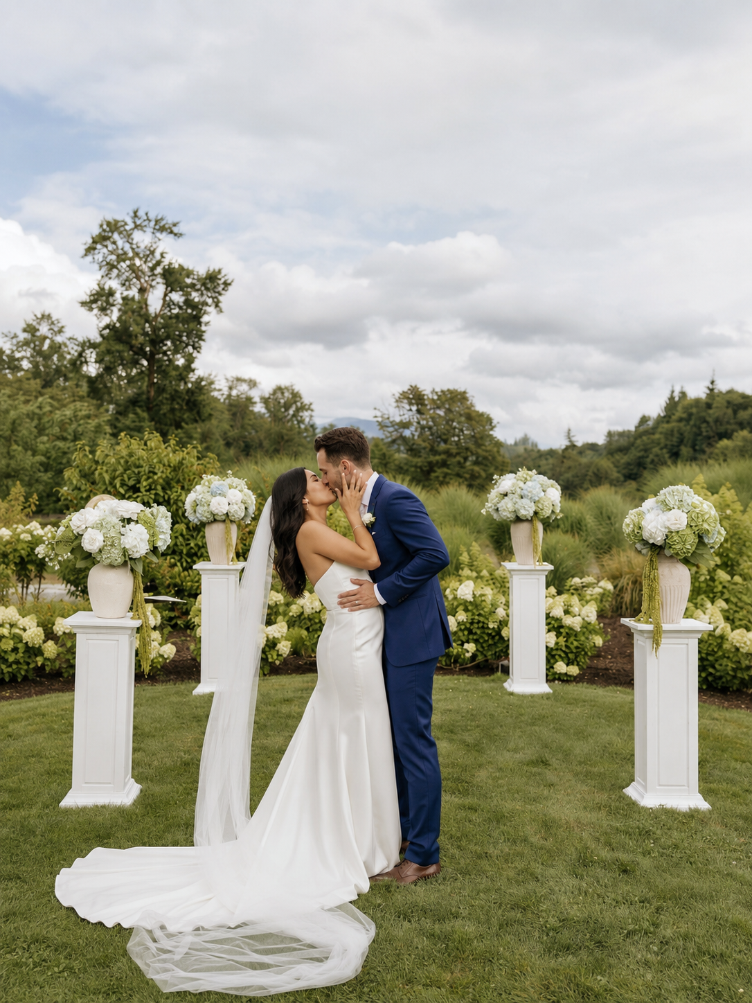 A couple sharing a kiss at their garden wedding surrounded by white florals