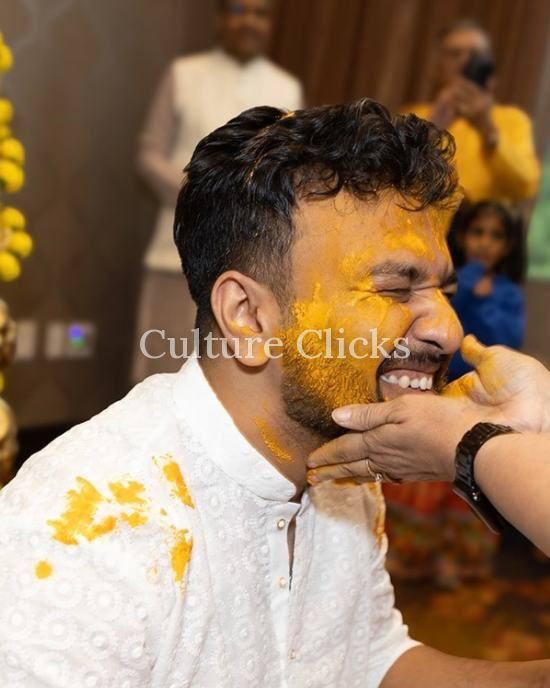 Groom laughing as family apply turmeric paste at his Haldi