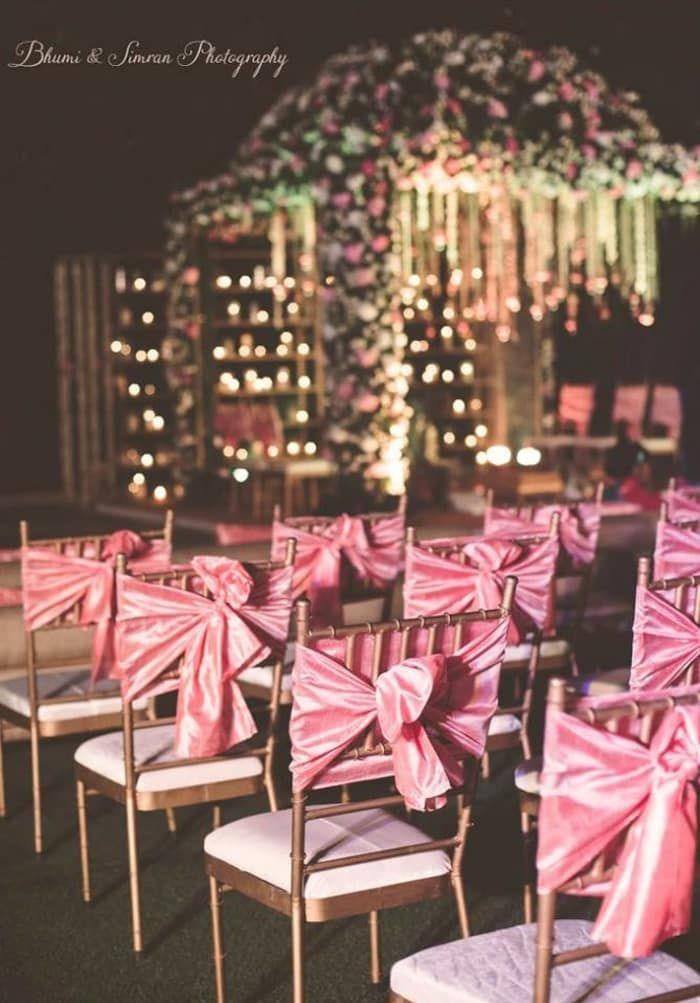 Ceremony chairs with pink satin sashes before a floral mandap