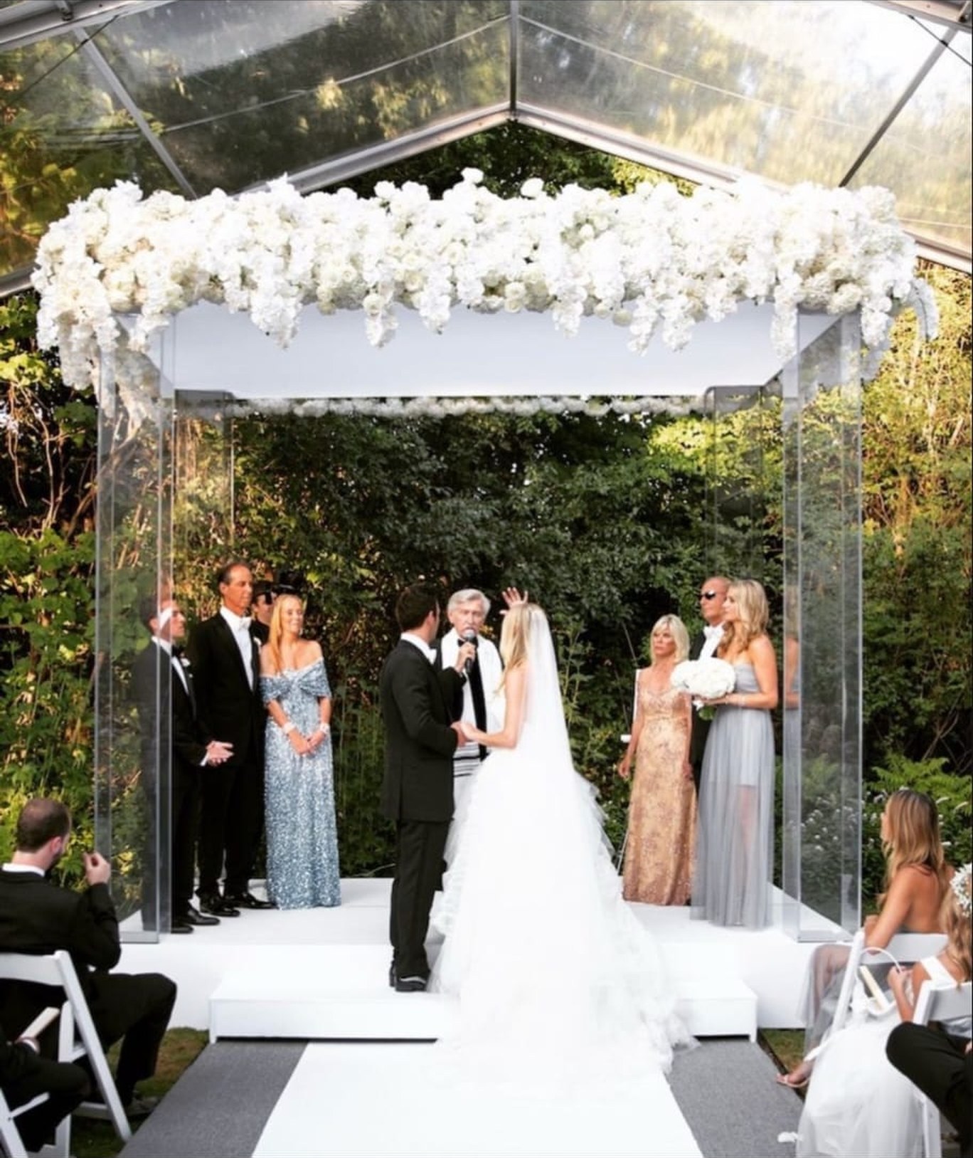 Clear acrylic mandap topped with white flowers set up for an outdoor ceremony