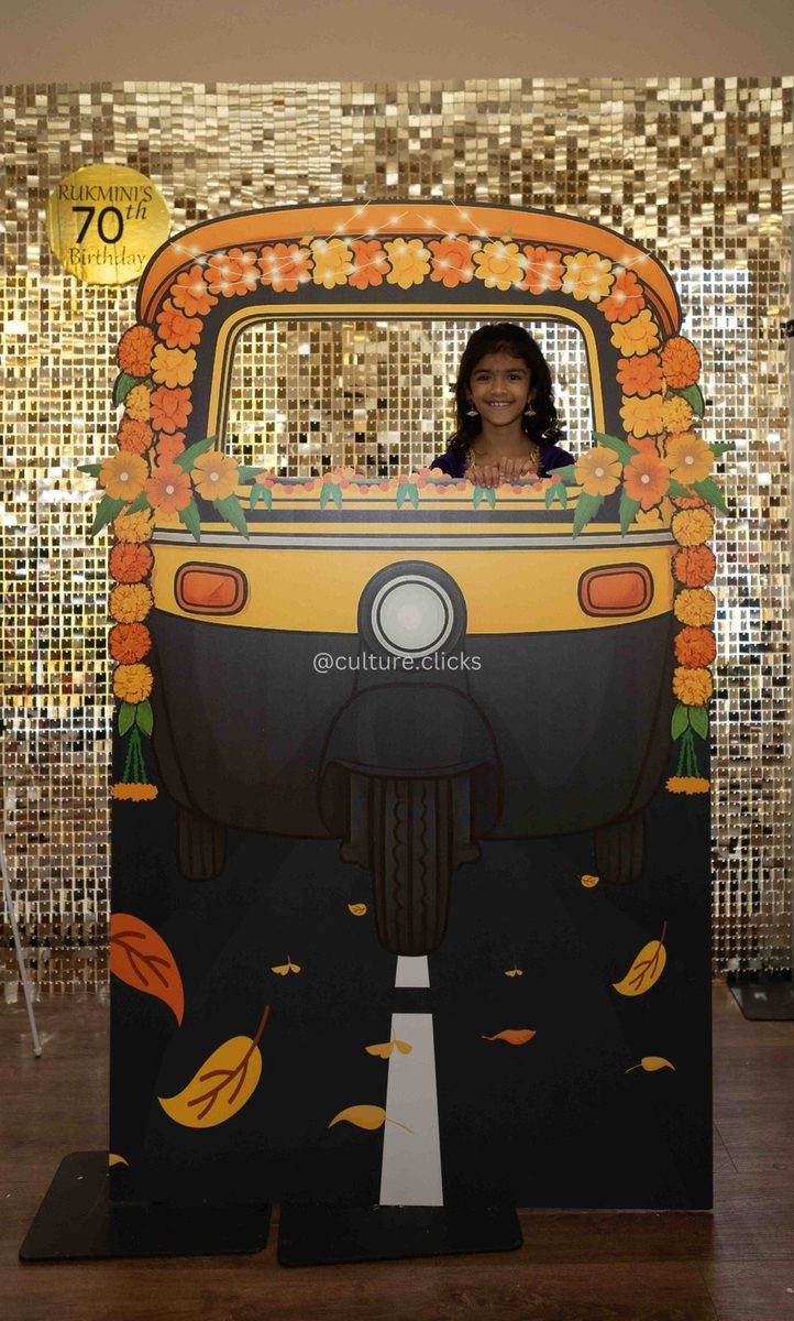 Auto-rickshaw photo cutout with marigold garlands in front of a gold sequin wall