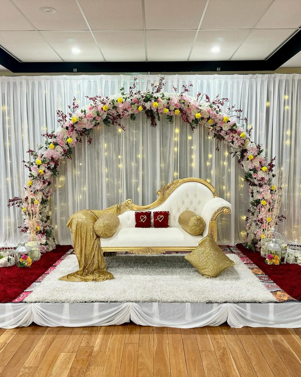 Round floral arch over a gold and white chaise on a red and white carpet stage with fairy lights