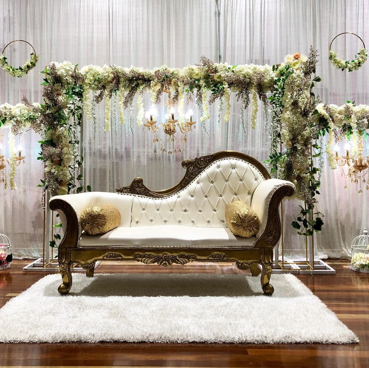 Gold chaise with a white and green floral frame, gold hoops and chandeliers