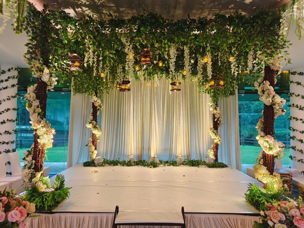 Mandap framed by tree-trunk pillars with white flowers, hanging greenery and lantern lights