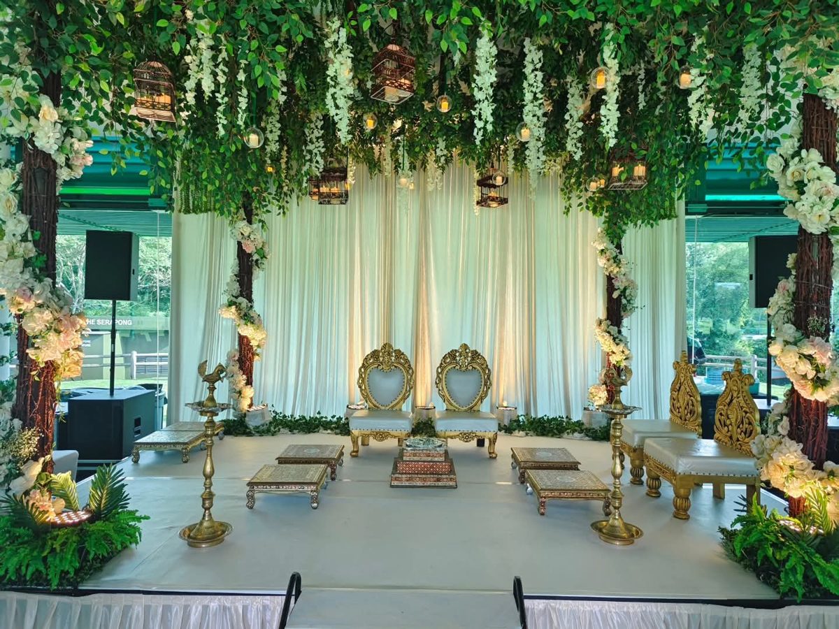 Wedding mandap under a canopy of hanging greenery and white wisteria with gold chairs and brass lamps