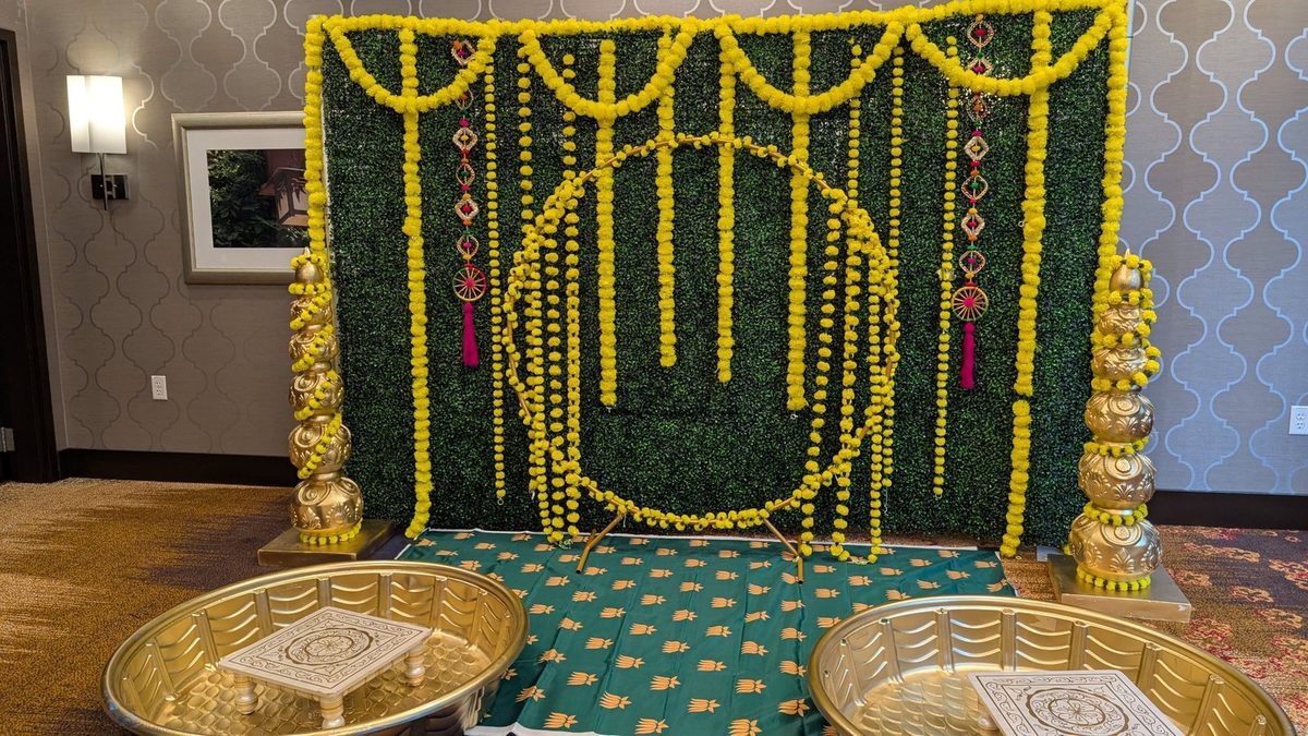 Green hedge wall with marigold garlands, gold ring and gold pillars