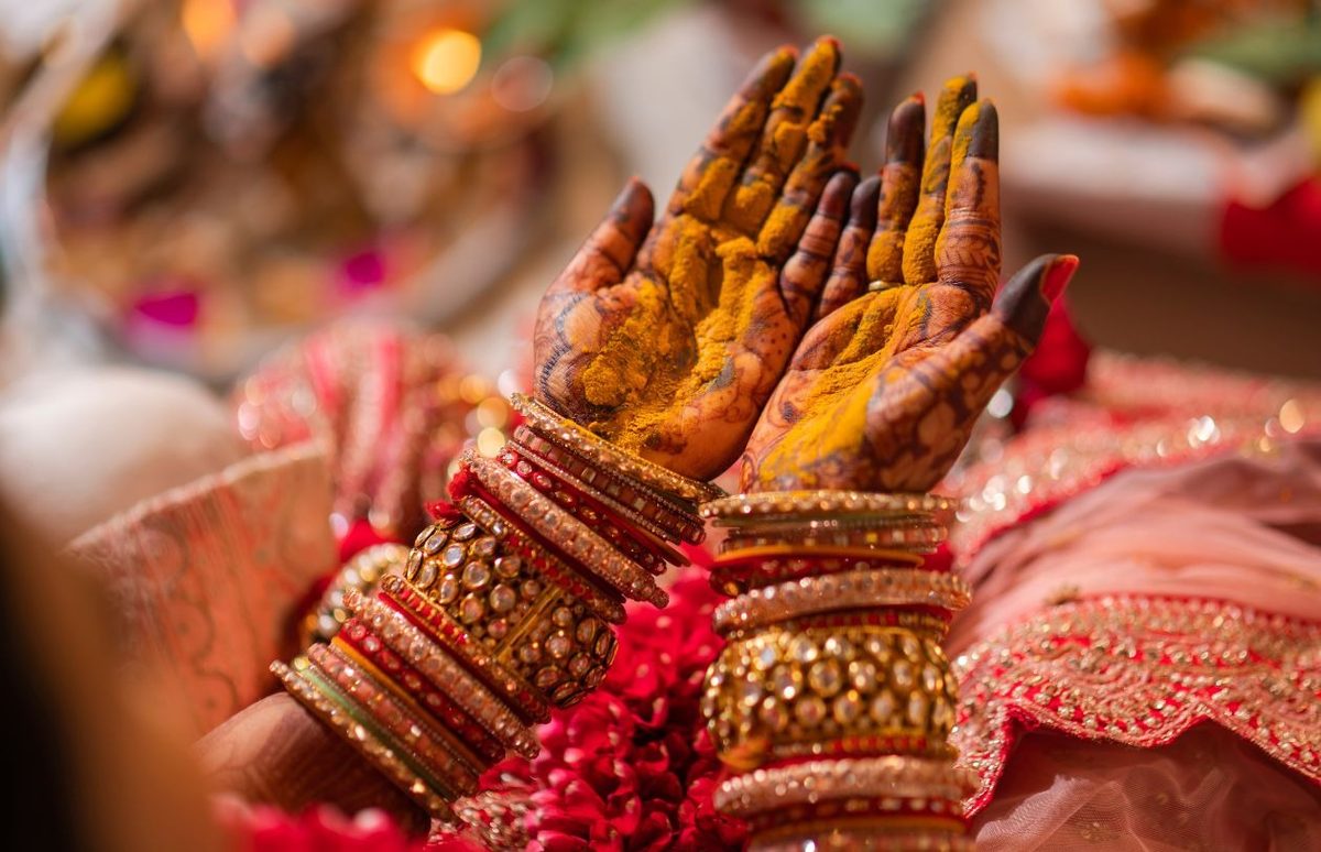 Hands with turmeric and mehndi wearing gold and red bangles during a Haldi ceremony