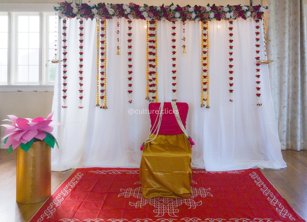 White drape backdrop with floral and jasmine hangings, a draped chair and a pink lotus