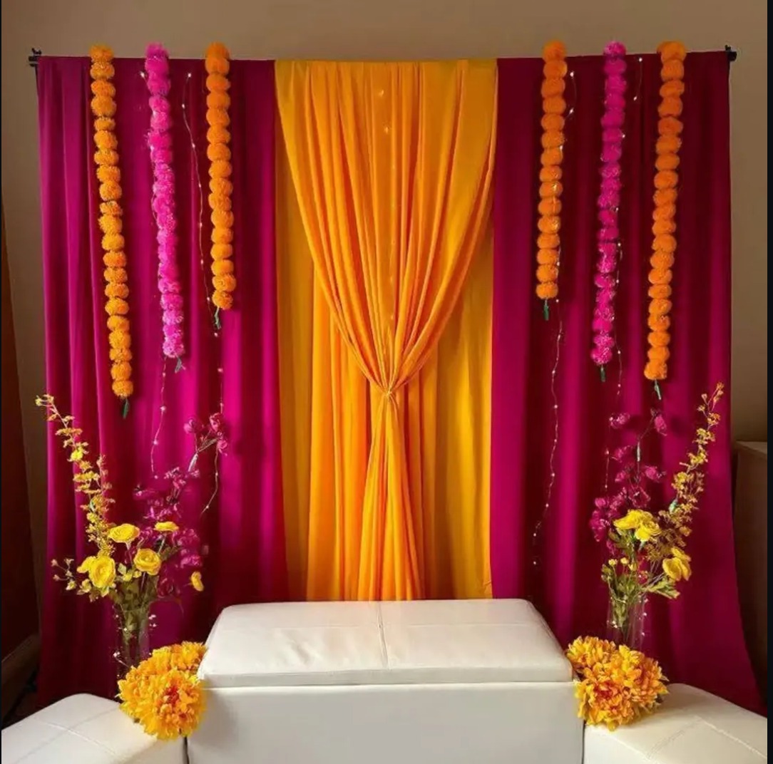 Magenta and yellow drapes with marigold garlands, flower vases and a white seating bench