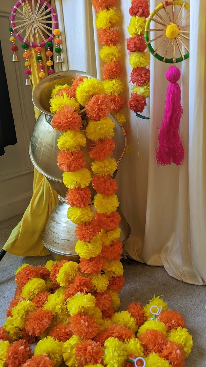 Orange and yellow marigold garland spilling from a brass pot beside hanging decor
