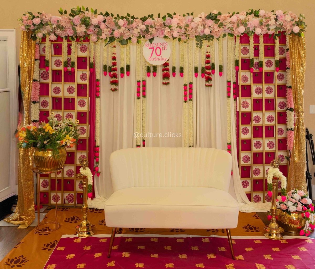 Pink and gold floral backdrop with a white sofa, brass lamps and a 70th birthday sign