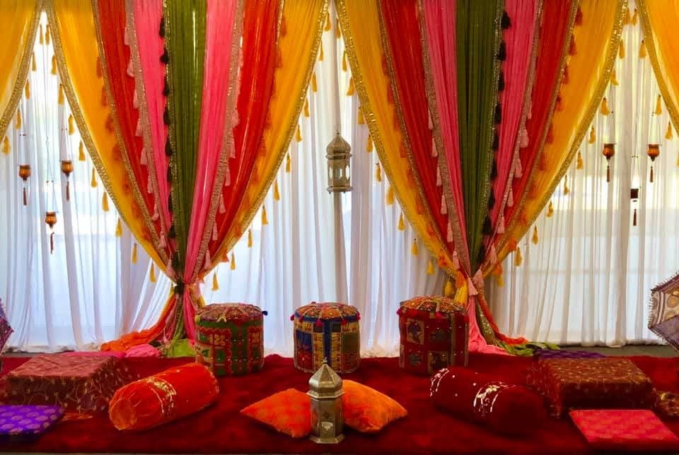Multicolour gota-edged drapes with tassels, floor cushions and poufs on a red carpet