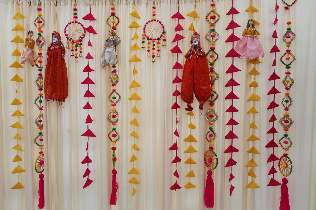 Hanging triangle garlands, gota ornaments and puppets on a cream curtain
