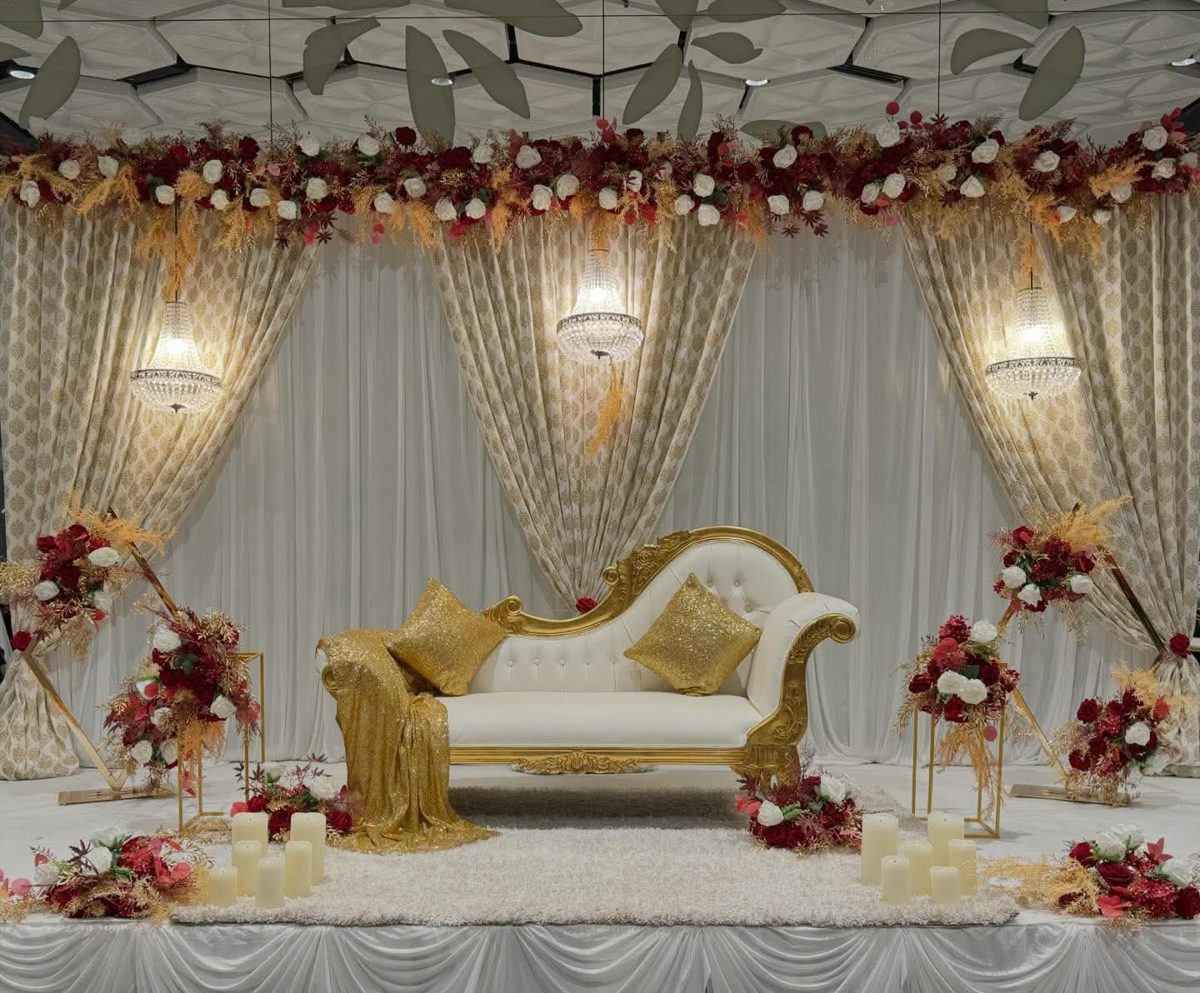 Gold chaise on a white stage with crystal chandeliers, gold-print drapes and red and white floral arrangements