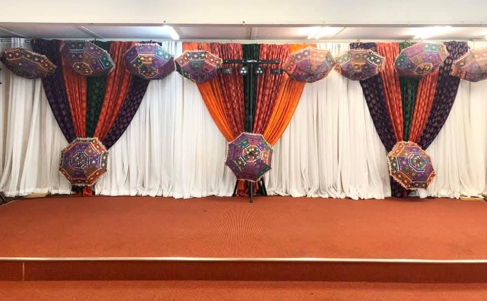 Stage backdrop with colourful embroidered umbrellas over orange, green and purple drapes