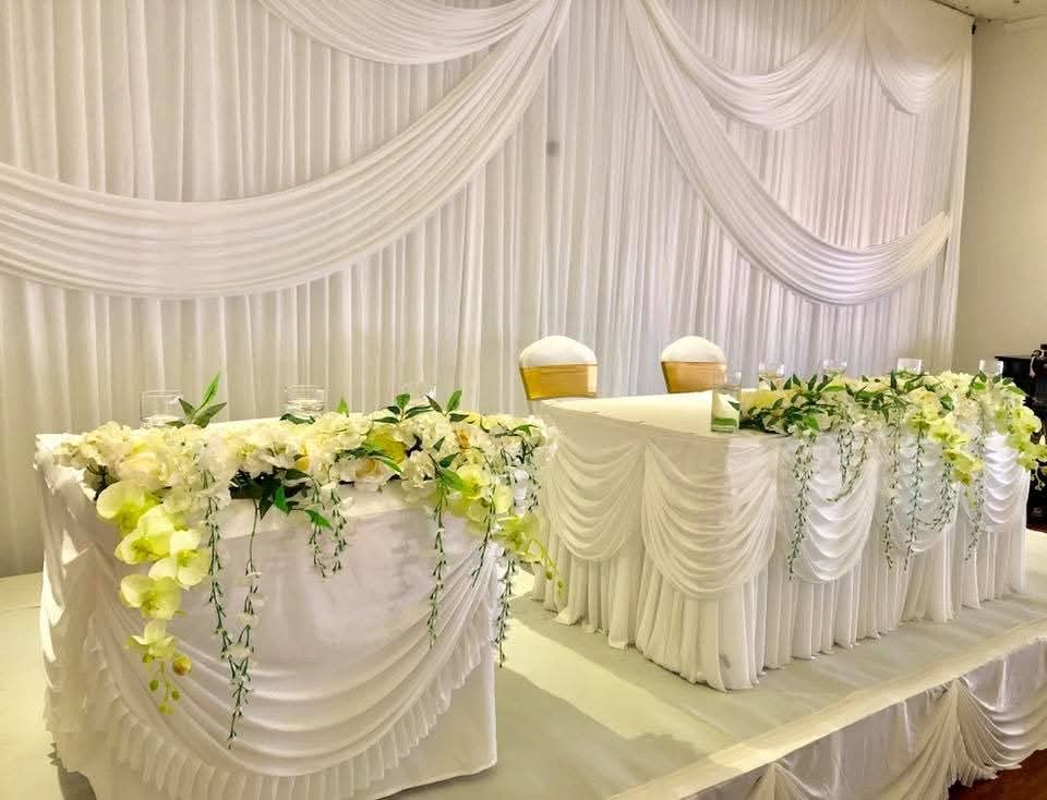 White draped reception head table with cascading white and green orchid arrangements and gold chair sashes