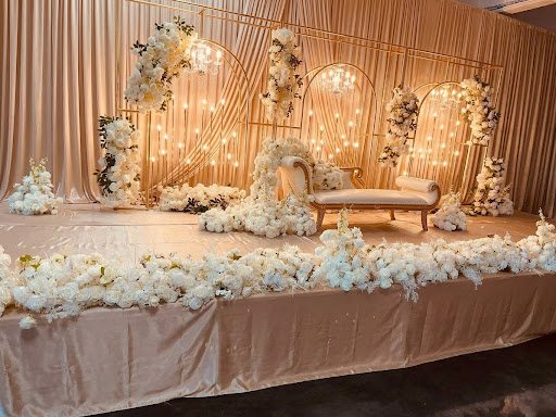 White floral reception stage with gold arches, a chaise lounge and warm candle lights