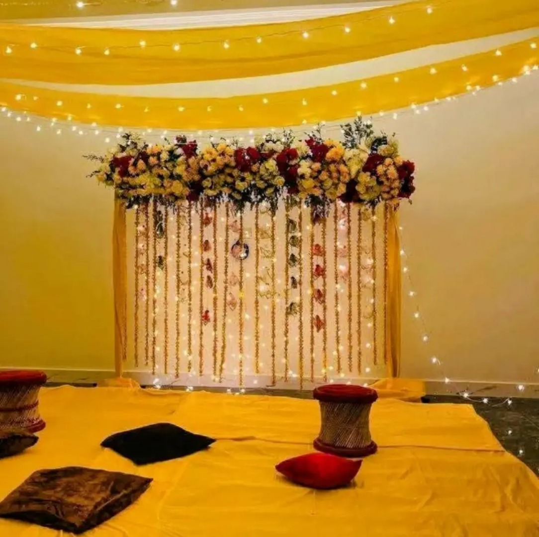 Yellow draped stage with a floral arrangement, garlands and fairy lights over floor seating